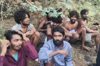 Tamil Nadu Police Eight men, appearing to be in their 20s, are sitting in a forest area after escaping a prison. Many of them are shirtless.