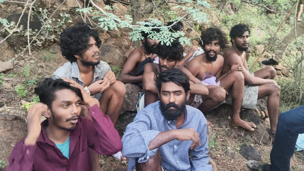 Tamil Nadu Police Eight men, appearing to be in their 20s, are sitting in a forest area after escaping a prison. Many of them are shirtless.