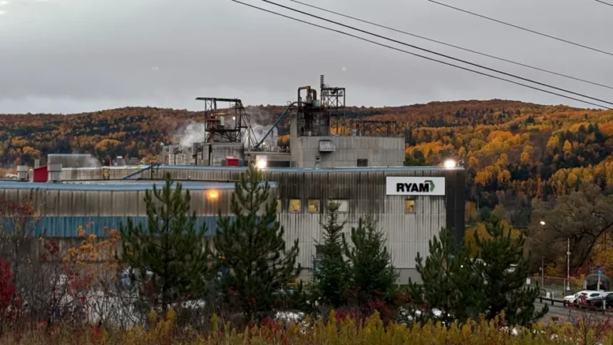 BBC/Jessica Murphy An image showing a part of the RYAM plant in Temsicaming, surrounded by red and orange fall trees. The building is grey with a sign in right corner that features the RYAM logo. Smoke is billowing out the ceiling.