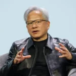 BBC Jensen Huang, the CEO of Nvidia, is seated in a grey armchair against a plain, light-blue background.