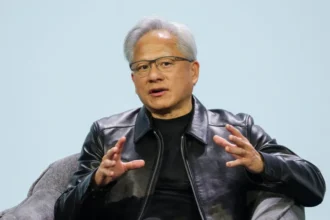 BBC Jensen Huang, the CEO of Nvidia, is seated in a grey armchair against a plain, light-blue background.
