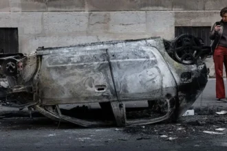 AFP via Getty Images A woman takes a photo of the wreckage of a burnt-out car in central Paris