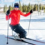 Adam Golebiewski Adam Golebiewski, a young man who has lost both legs, on skis in snow, he is smiling at the camera.