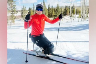 Adam Golebiewski Adam Golebiewski, a young man who has lost both legs, on skis in snow, he is smiling at the camera.