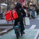 Michael Nagle/Bloomberg via Getty Images A delivery worker dressed in black rides a bike with a DoorDash bag in New York.