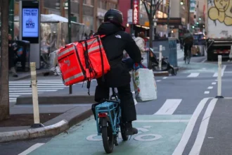 Michael Nagle/Bloomberg via Getty Images A delivery worker dressed in black rides a bike with a DoorDash bag in New York.