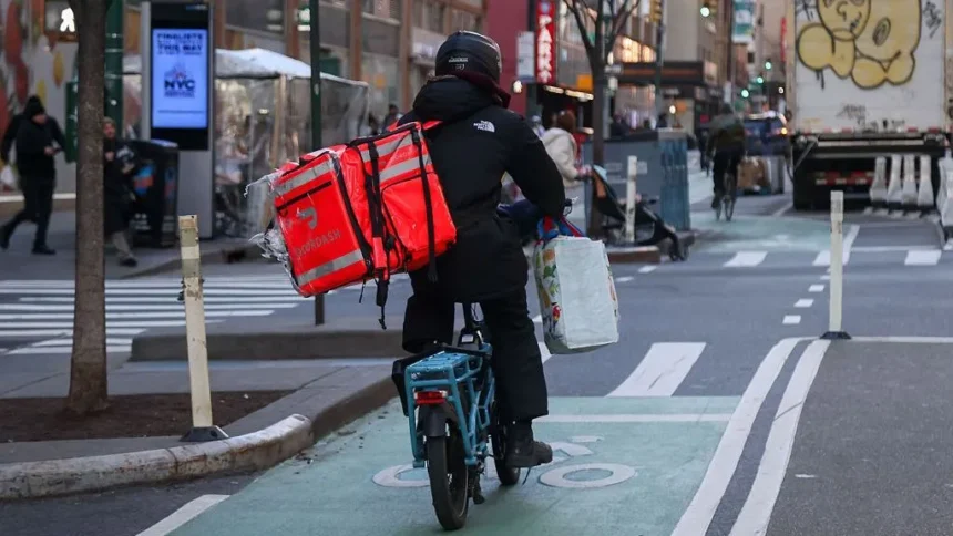 Michael Nagle/Bloomberg via Getty Images A delivery worker dressed in black rides a bike with a DoorDash bag in New York.