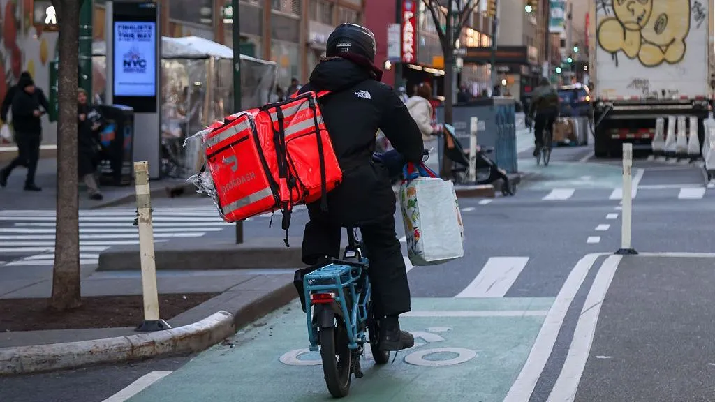 Michael Nagle/Bloomberg via Getty Images A delivery worker dressed in black rides a bike with a DoorDash bag in New York.