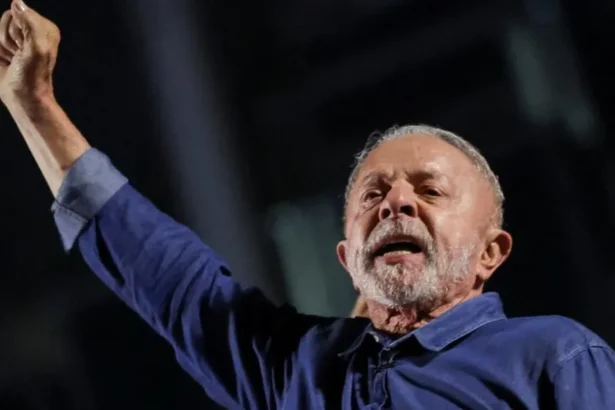 Reuters President Lula extends his right arm, his hand in a fist, as he reacts to his election. He is wearing a blue denim shirt, and has short grey hair and beard.