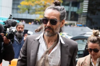 PA Russell Brand arrives at Southwark Crown Court, alongside his wife, wearing sunglasses and with his hair tied up, as cameras fix upon him