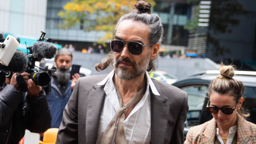 PA Russell Brand arrives at Southwark Crown Court, alongside his wife, wearing sunglasses and with his hair tied up, as cameras fix upon him
