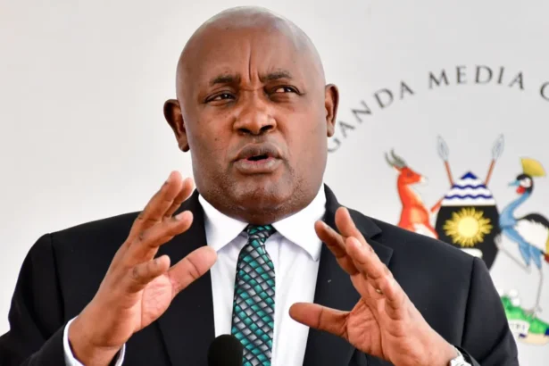 Reuters Uganda's Health Minister Chris Baryomunsi, in black suit and white shirt, gestures as he speaks. There is a black microphone in front of him and a banner with words Uganda Media Centre and a Ugandan coat of arms behind him.