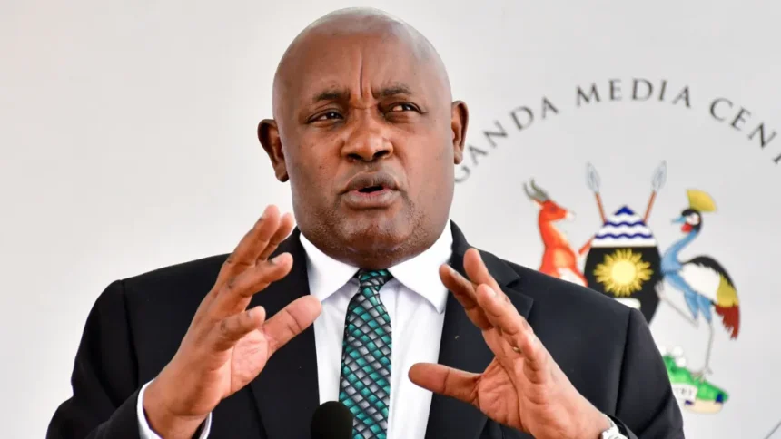 Reuters Uganda's Health Minister Chris Baryomunsi, in black suit and white shirt, gestures as he speaks. There is a black microphone in front of him and a banner with words Uganda Media Centre and a Ugandan coat of arms behind him.