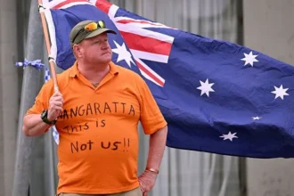 Getty Images A man wearing an orange t-shirt reading "Wangaratta this is not us!!" waves an Australian flag