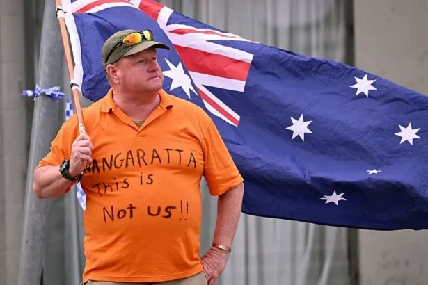 Getty Images A man wearing an orange t-shirt reading "Wangaratta this is not us!!" waves an Australian flag