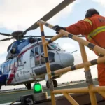 Getty Images A helicopter lands on an oil rig and a man in orange overalls is climbing up steps and heading towards it