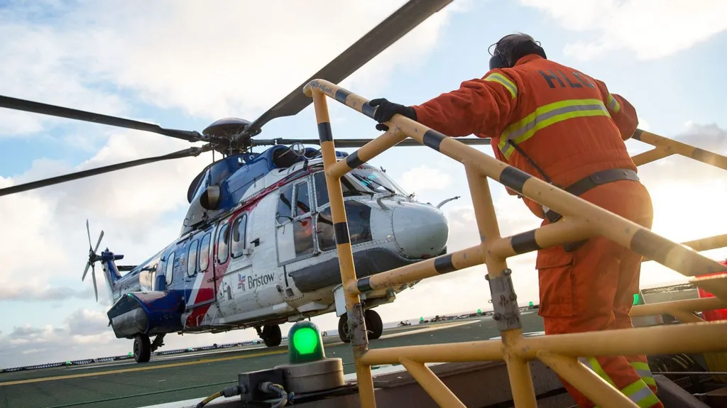 Getty Images A helicopter lands on an oil rig and a man in orange overalls is climbing up steps and heading towards it