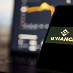 Bloomberg via Getty Images A phone propped up in front of a laptop. On the phone screen it says Binance and the blurred laptop screen shows a bar chart