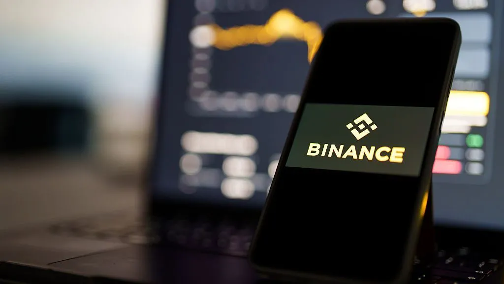 Bloomberg via Getty Images A phone propped up in front of a laptop. On the phone screen it says Binance and the blurred laptop screen shows a bar chart