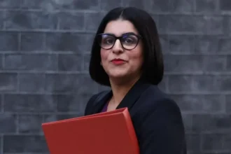 EPA Home Secretary Shabana Mahmood carries a red folder as she walks past a grey brick wall.