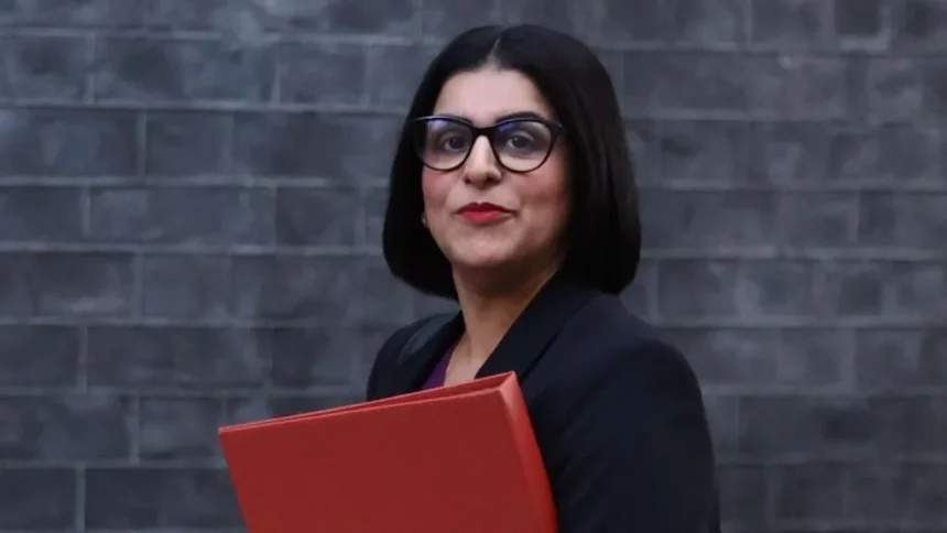 EPA Home Secretary Shabana Mahmood carries a red folder as she walks past a grey brick wall.