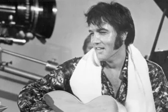 Getty Images Elvis holding a guitar in a black and white photo from a studio set in 1973