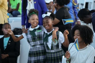 Reuters Primary students smile and hold flags of the Bahamas ahead of a youth rally with Britain's King Charles at Clifford Park