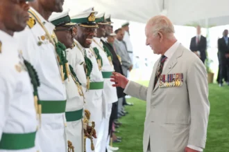 Press Association King Charles, wearing a light beige suit with military medals displayed speaks to veterans wearing white uniforms highlighted with green