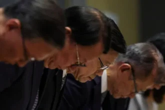 Reuters A row of Chinese men wearing dark suits and glasses bow in apology, with the focus of the shot centering on John Lee in the middle of the row