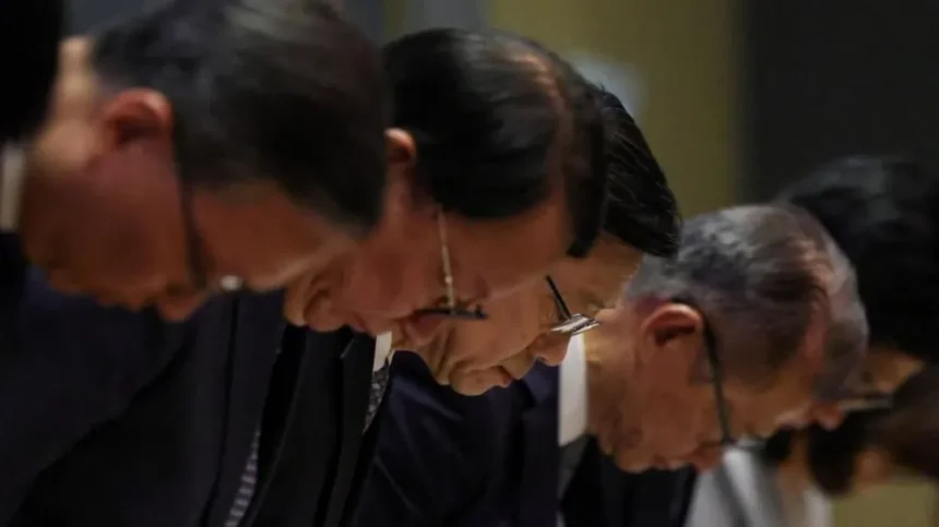 Reuters A row of Chinese men wearing dark suits and glasses bow in apology, with the focus of the shot centering on John Lee in the middle of the row