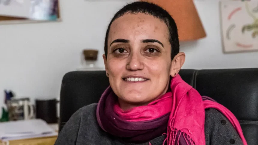 AFP via Getty Images Egyptian journalist Lina Attalah sits on a black leather chair. She has a red scarf around her neck, a grey top, cropped black hair, stud earrings and and a silver metal studd in her right nostril, a broad smile on her lips.