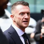 Reuters Tommy Robinson is walking towards the court, smartly dressed, surrounded by people, some filming him with cameras.
