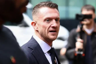 Reuters Tommy Robinson is walking towards the court, smartly dressed, surrounded by people, some filming him with cameras.