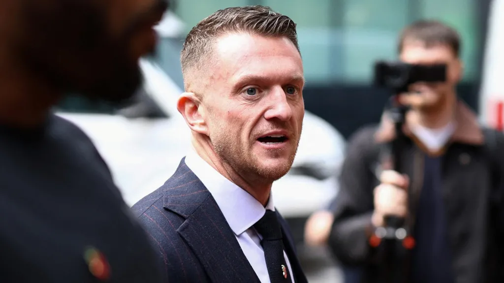 Reuters Tommy Robinson is walking towards the court, smartly dressed, surrounded by people, some filming him with cameras.